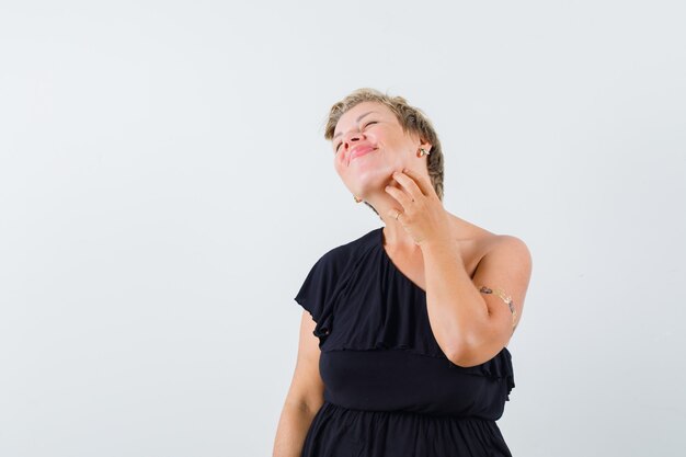 Glamorous woman scratching her chin in black blouse and looking relaxed 