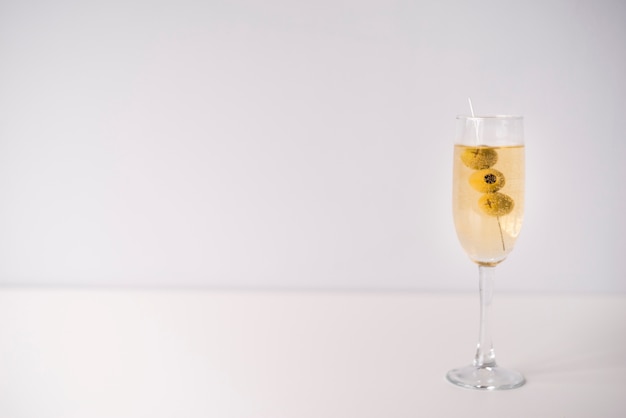 Glass of alcoholic drink with olives on white background