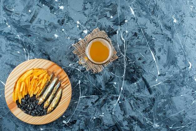 A glass of beer on texture and appetizers on wooden plate, on the blue table. 