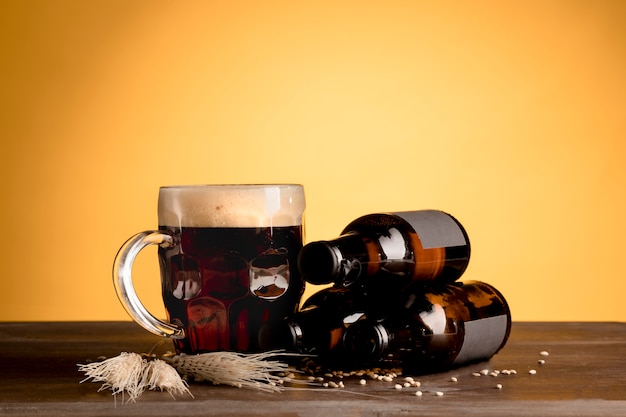 Free photo glass of beer with foam and bottles of beer on wooden table