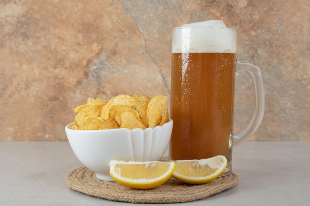 Glass of beer with lemon slices and bowl of chips on stone table