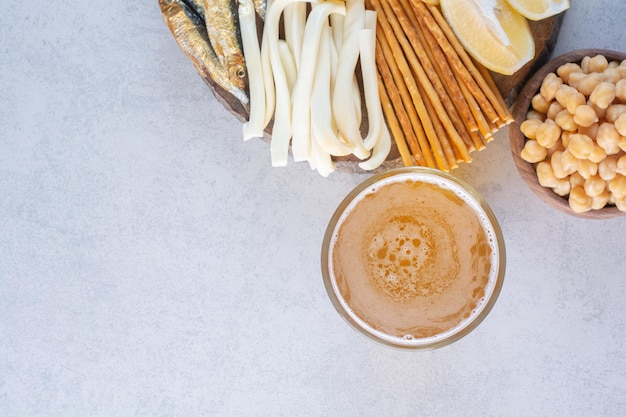 A glass of beer with peas and fish on wooden plate