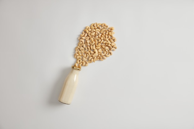 Glass bottle of cold cashew milk next to pile of nuts on white background. Nutrient organic non diary beverage for vegans. Healthy homemade drink to substitute cows milk. Dairy free alternative.