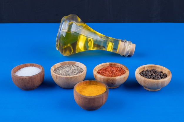 Glass bottle of extra virgin oil and various spices on blue surface