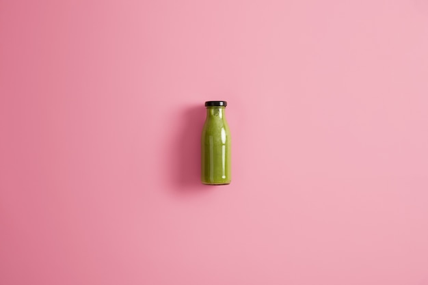 Free photo glass bottle of refreshing smoothie made of spinach, cucumber and avocado, low in calories, isolated on pink background. dieting and healthy lifestyle concept. blended green vegetables for drink