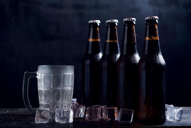 Glass bottles of beer with glass and ice on dark background