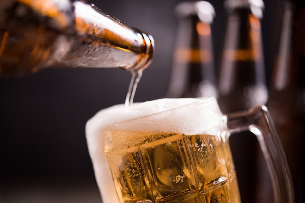 Glass bottles of beer with glass and ice on dark background