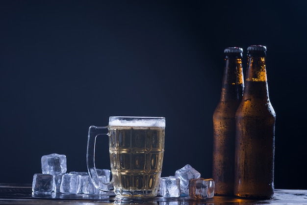 Free Photo glass bottles of beer with glass and ice on dark background