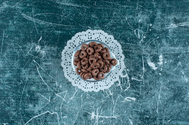 A glass bowl of corn rings on caster , on the blue table. 