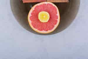 Free photo glass bowl of fresh grapefruit slice with lemon on stone table.