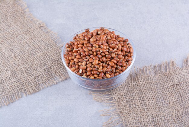 Glass bowl on two pieces of fabric, filled with red beans on marble surface