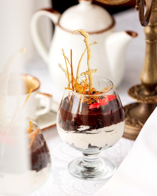 A glass of chocolate dessert with vanilla cream garnished with caramel decoration and flower