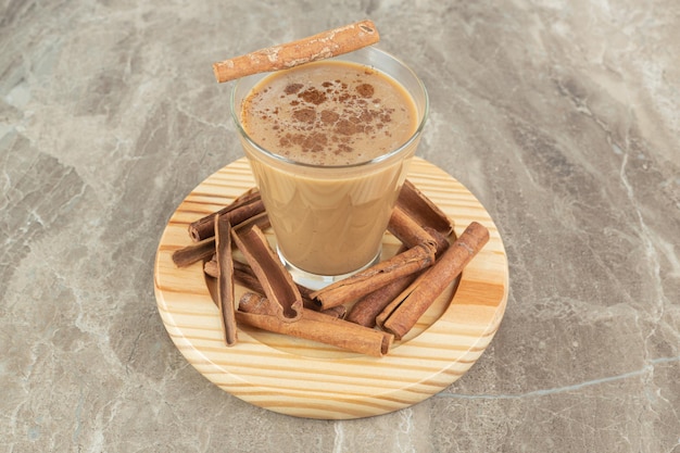 Glass of coffee with cinnamons on wooden board