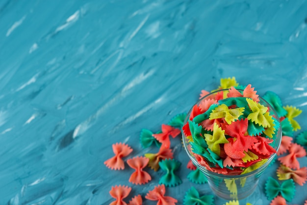 Free photo glass of colorful raw farfalle pasta on blue background.