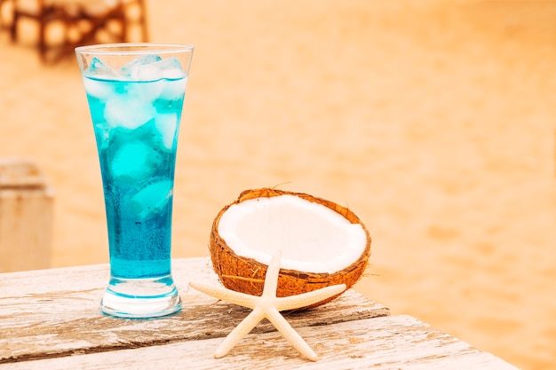 Free Photo glass of cooling blue drink and cracked coconut wooden table