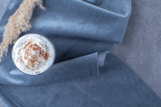 Free photo glass cup of coffee latte on piece of fabric next to pampas grass, on the blue table.