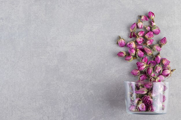 A glass cup full of dried rose flower buds placed on stone background. 