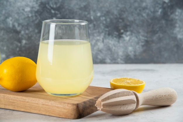 A glass cup of lemonade and wooden reamer.