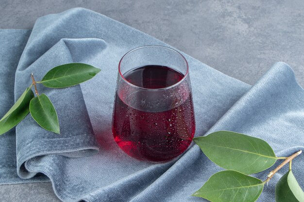 A glass cup of pomegranate juice with ice cubes on a tablecloth