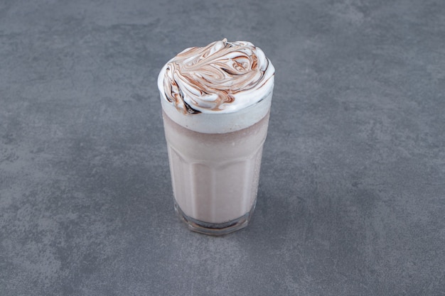 A glass cup of sweet milkshake with whipped cream . 