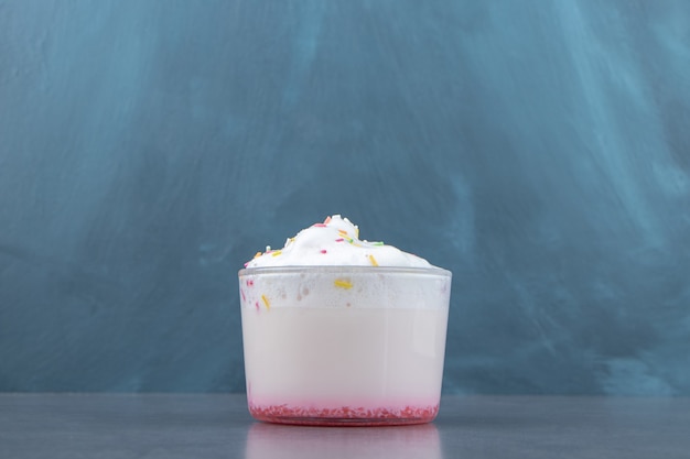 A glass cup of sweet milkshake with whipped cream . 