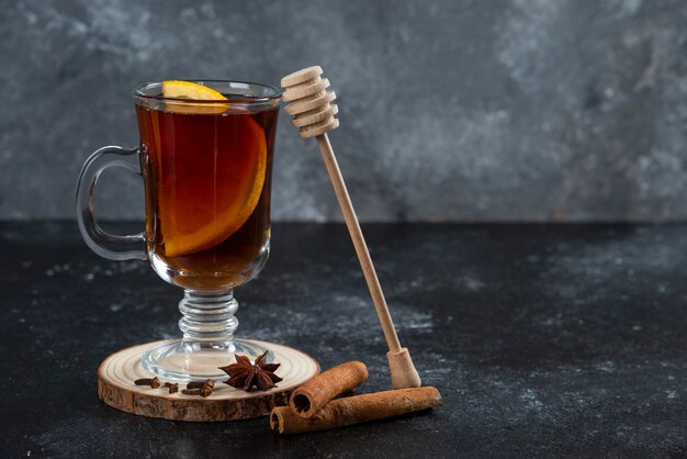 A glass cup of tea and with cinnamon sticks and wooden dipper.