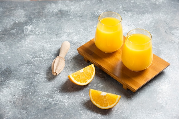 Glass cups of orange juice and a wooden reamer .