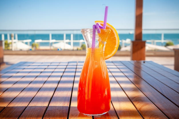 A glass of fruit juice on the ground with beach, side view.