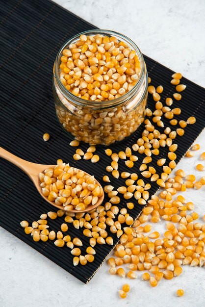 Glass jar of corn kernels with spoon on black cutting board.