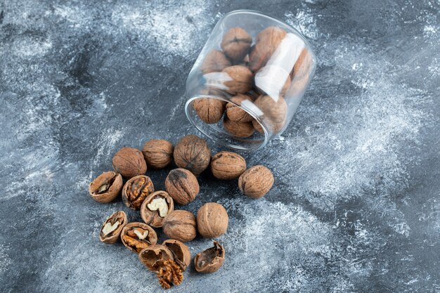 A glass jar full of healthy walnuts on a gray surface.