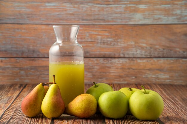 A glass jar of juice with green apples and pears around