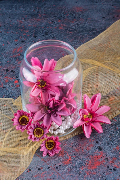 Free Photo a glass jar of purple flowers with pearls on yellow tablecloth .