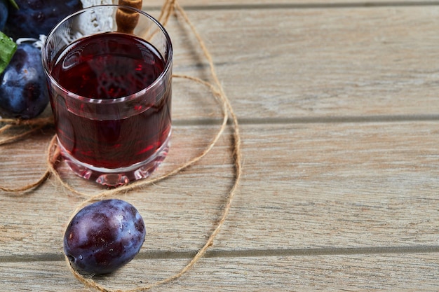 A glass of juice and garden plums on wooden table.