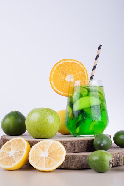 A glass of juice with fruit slices and fresh fruits.