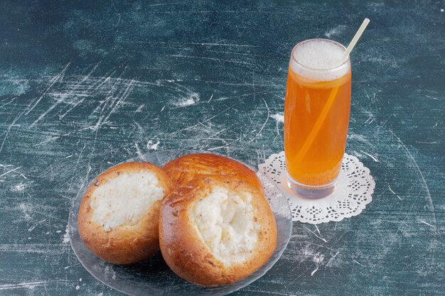 A glass of lemonade and cheese buns on marble table.