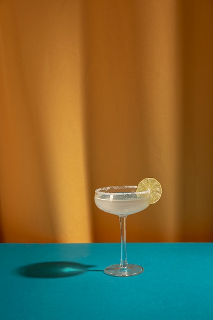 Free Photo glass of margarita cocktail garnish with lime on blue table against yellow curtain