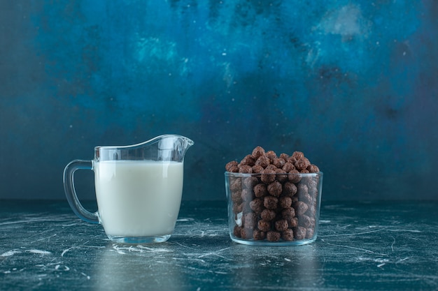 Free photo a glass of milk next to corn balls in a glass bowl , on the blue background. high quality photo