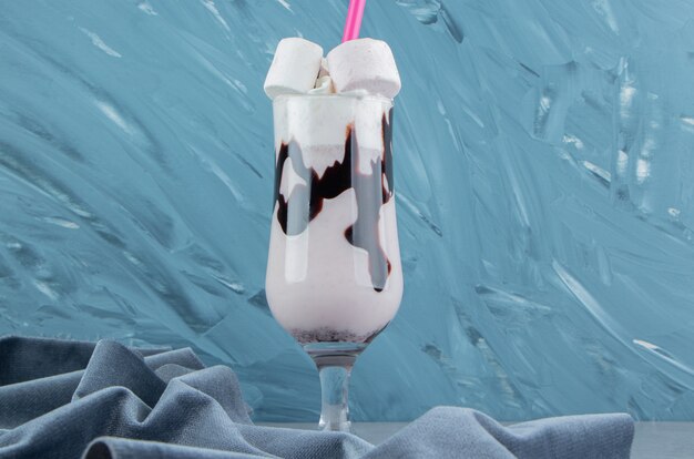 A glass of milkshake next to the towel , on the blue background. High quality photo