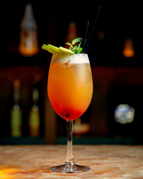 A glass of orange cocktail garnished with mint and green apple slices