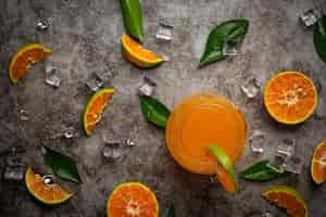 Free photo a glass of orange juice and fresh fruit on the floor with ice cubes.