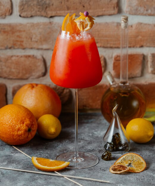 A glass of orange red cocktail with orange slices on the top.