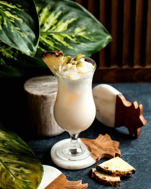 Free photo a glass of pineapple milkshake topped with whipped cream kiwi and pineapple