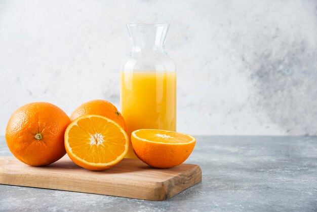 Glass pitcher of juice with sliced orange fruit on a wooden board .