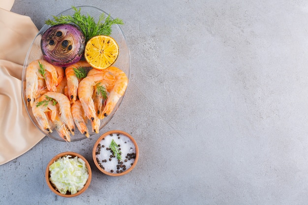 Free photo a glass plate of delicious shrimps with sliced lemon and onion on a stone surface