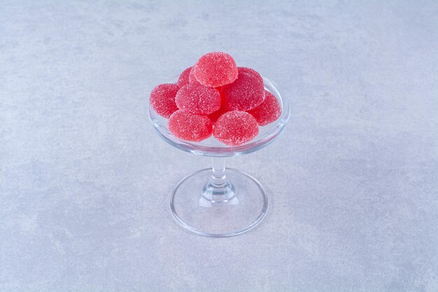 A glass plate full of red sugary fruit jelly candies on gray table. 