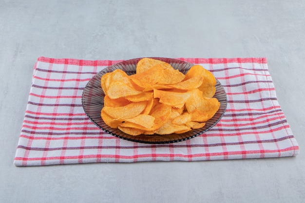 Glass plate of spicy chips placed on stone.