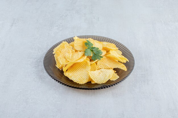 Glass plate of tasty ripple chips on stone.