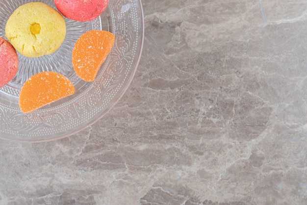 Glass platter with cookies and jelly sweets on marble surface