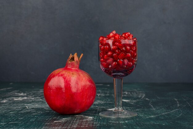 Glass of pomegranate seeds and pomegranate on marble surface