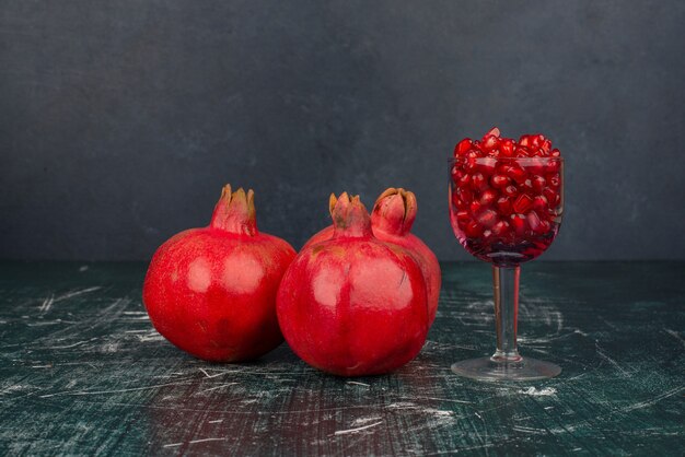 Glass of pomegranate seeds and pomegranate on marble surface.